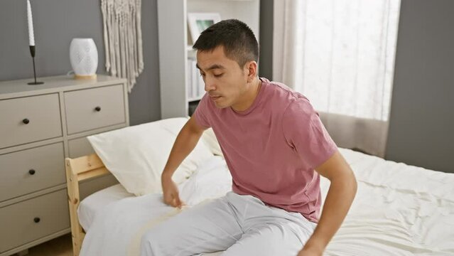 A contemplative young hispanic man sits in a modern bedroom, evoking themes of relaxation and urban living.