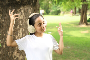 Portrait of Indian girl child lost in music in calm green city park using headphones early morning...