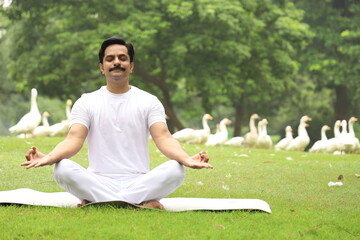 Happy Indian man doing yoga early morning in a tranquil environment surrounded with lush green serene atmosphere. high concentration level. 