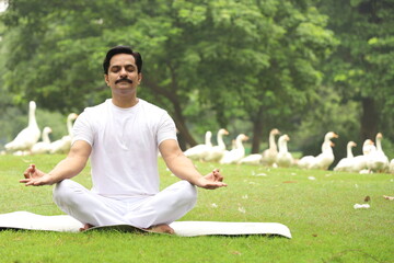 Happy Indian man doing yoga early morning in a tranquil environment surrounded with lush green serene atmosphere. high concentration level. 