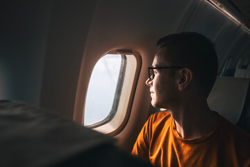 Portrait of man traveling by airplane. Passenger looking through plane window during flight..