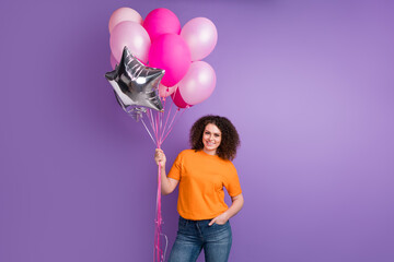Photo of good mood adorable woman wear orange t-shirt holding big balloons bouquets isolated purple color background