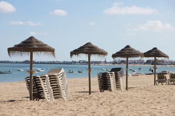 Straw umbrellas and sun loungers on the beach on a sunny day. The concept of rest and relaxation, holidays and travel. In the background the fishermen's boats.