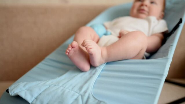 Newborn baby lies in a cocoon baby lounger in a light bodysuit, close-up of his legs. Happy children morning,wellness and development at home