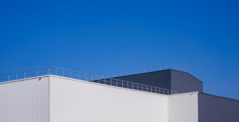 Modern white and black aluminium corrugated factory buildings with steel fence on rooftop against...