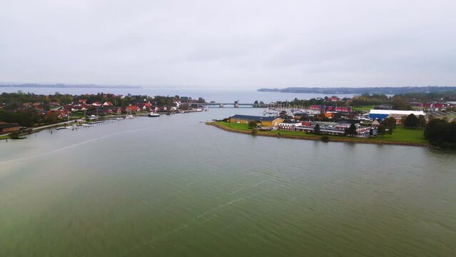 Drohnenaufnahme eines malerischen K&uuml;stendorfes mit Hafen und &ouml;ffnenden Schleusentoren bei bedecktem Himmel. Marina Toft und Egernsundbr&uuml;cke in Egernsund, D&auml;nemark.