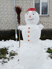 A snowman in the yard near the house is molded by children from fresh snow and a carrot instead of...