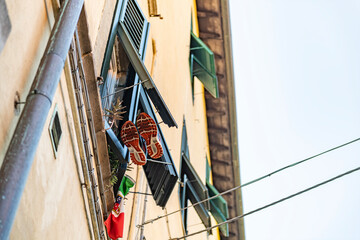 Originelle Perspektive aus einer Gasse in Pisa. An einem Fenster hängen Schuhe und eine italienische Flagge, Italien