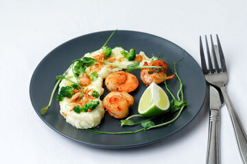Scallops served with garnish mashed potatoes on black plate with fork and knife on white background. Top View.