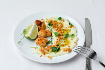 Scallops served with garnish mashed potatoes on the plate with fork and knife isolated on white background. Side View.
