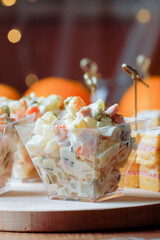 Russian traditional salad olivier with pea in portion glass on fest table oranges and appetizers background. Side view. Vertical orientation.