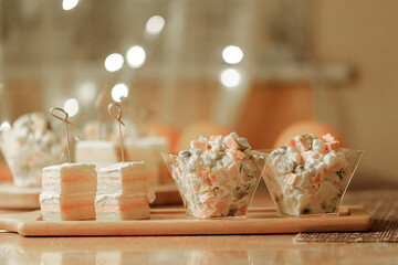 Russian traditional salad olivier with pea in portion glass on fest table oranges and appetizers background. Side view.
