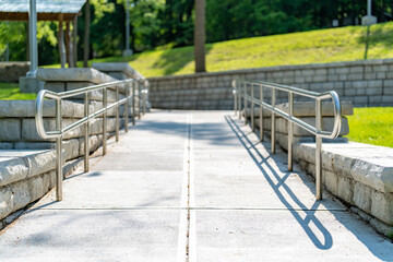 Outdoor, exterior gray concrete ramped sidewalk with stainless steel railings. 