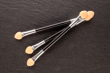 Three cosmetic applicators on slate stone, macro, top view.