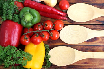 There are wooden spoons with different vegetables on a wooden table.