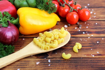 On a wooden background lies a wooden spoon with dry pasta in a semicircle.