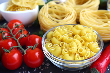 On a black stone board lie different pasta in plates, pasta nests and vegetables.