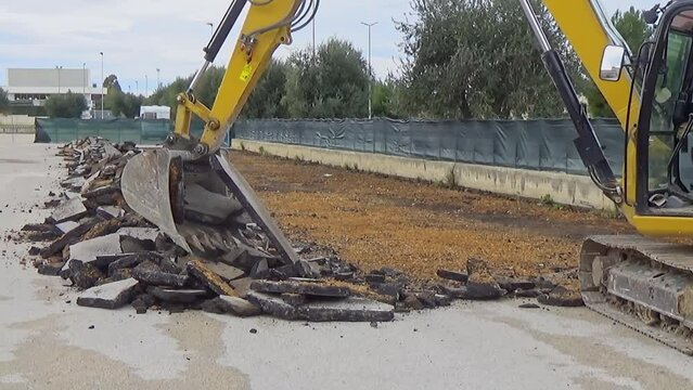 Excavator with bucket demolishes the asphalt layer of a road.