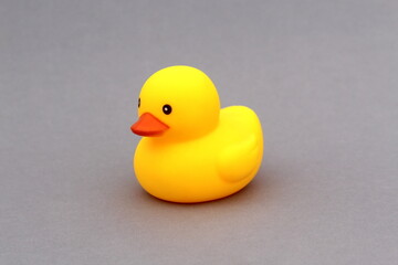 A yellow rubber duck toy stands on a gray background.	