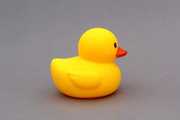 A yellow rubber duck toy stands on a gray background.