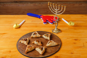 Sweet gomentashi cookies on a wooden board next to a clapper and a menorah for the holiday of Purim