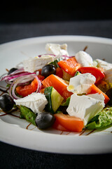 Greek salad closeup with feta cheese, Kalamata olives, and balsamic glaze on a white plate