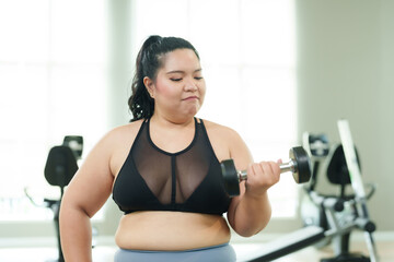 Plus-size Asian woman exercise in gym, Focused in activewear, exuding confidence and dedication in workout. Concentrated female doing arm exercises with weights, showing commitment to fitness against