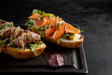 Bruschetta set with salmon, roast beef, and tuna on a black rectangular plate