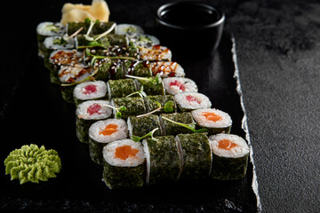 Assorted hosomaki sushi set with salmon, tuna, eel, and cucumber on black textured background