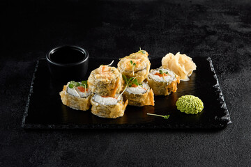 Salmon tempura roll on a textured black slate with condiments