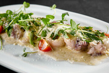 Creamy seafood assortment garnished with fresh greens and cherry tomatoes on a white oval plate