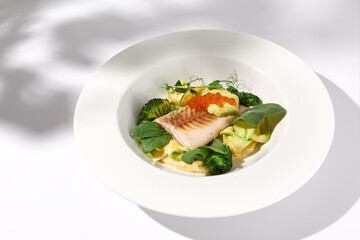 Cod fillet with caviar and zucchini-broccoli garnish, side view on white plate with delicate leaf shadow
