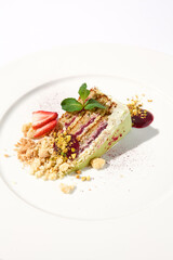 Pistachio cake with a raspberry layer and crumbled cookie and pistachio topping on an isolated white background