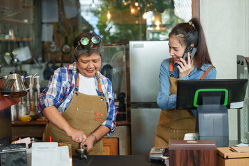 Businessman, cafe owner, beautiful Asian woman Wearing navy blue shirt. Hand taking coffee order phone behind cash registe counter single mother pension making coffee. bakery small family business.