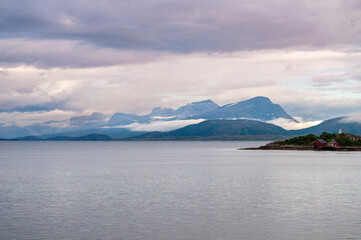 Irradiated water in the sea in a fjord in Norway. Snowy high mountains in the clouds at sunset.