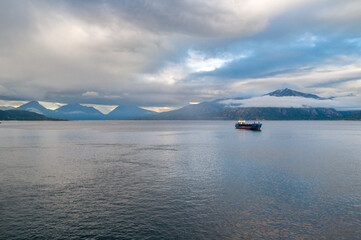 Sunset and illuminated clouds with mountains in a fjord in Norway. A cargo ship floats on the surface of the sea in the north of Europe.