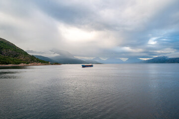 Sunset and illuminated clouds with mountains in a fjord in Norway. A cargo ship floats on the surface of the sea in the north of Europe.
