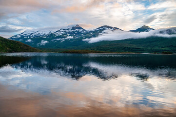 Naklejka premium Irradiated water in the sea in a fjord in Norway. Snowy high mountains in the clouds at sunset.