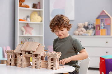 Little boy playing with wooden entry gate at white table in room. Child's toy