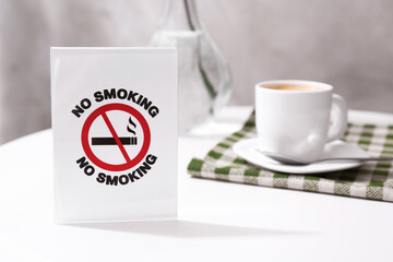 No Smoking sign and cup of coffee on white table indoors