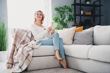 Fototapeta premium Full length photo of minded smart person sit barefoot comfy couch hold notepad look interested away fantasize flat indoors