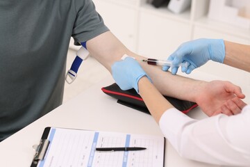 Doctor taking blood sample from patient with syringe at white table in hospital, closeup - obrazy, fototapety, plakaty
