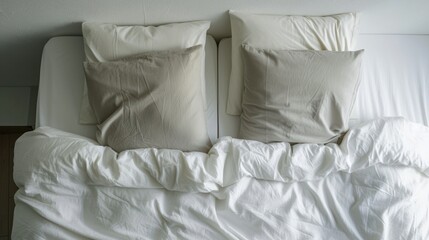 two pillows sitting on top of a bed with a white comforter and a white pillow on the bottom of the bed.