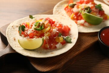 Delicious tacos with vegetables, lime and ketchup on wooden table, closeup