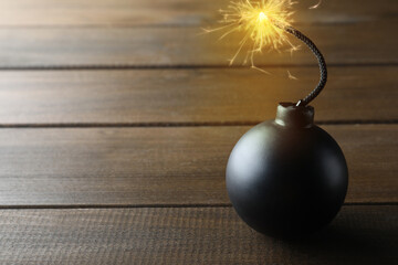 Old fashioned black bomb with lit fuse on wooden table, space for text