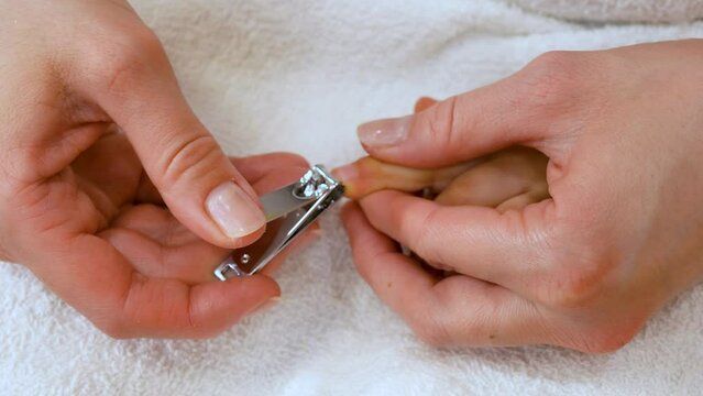 Close-up shot of a mother gently holding her little child's foot and cutting toenails on white towel.