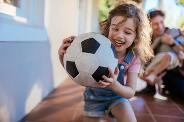 Joyful girl playing with a soccer ball with her family in the background