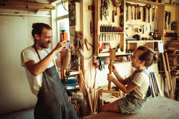 Father taking a photo of his daughter in a woodworking workshop