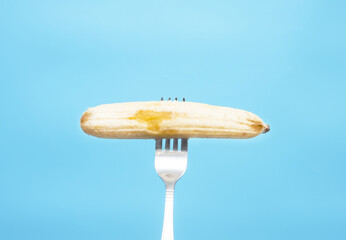 Banana on a fork on a blue background. Copy space. Ripe delicious banana pricked on a kitchen fork