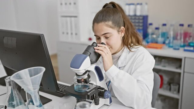 Young hispanic woman scientist analyzing samples with a microscope in a laboratory environment